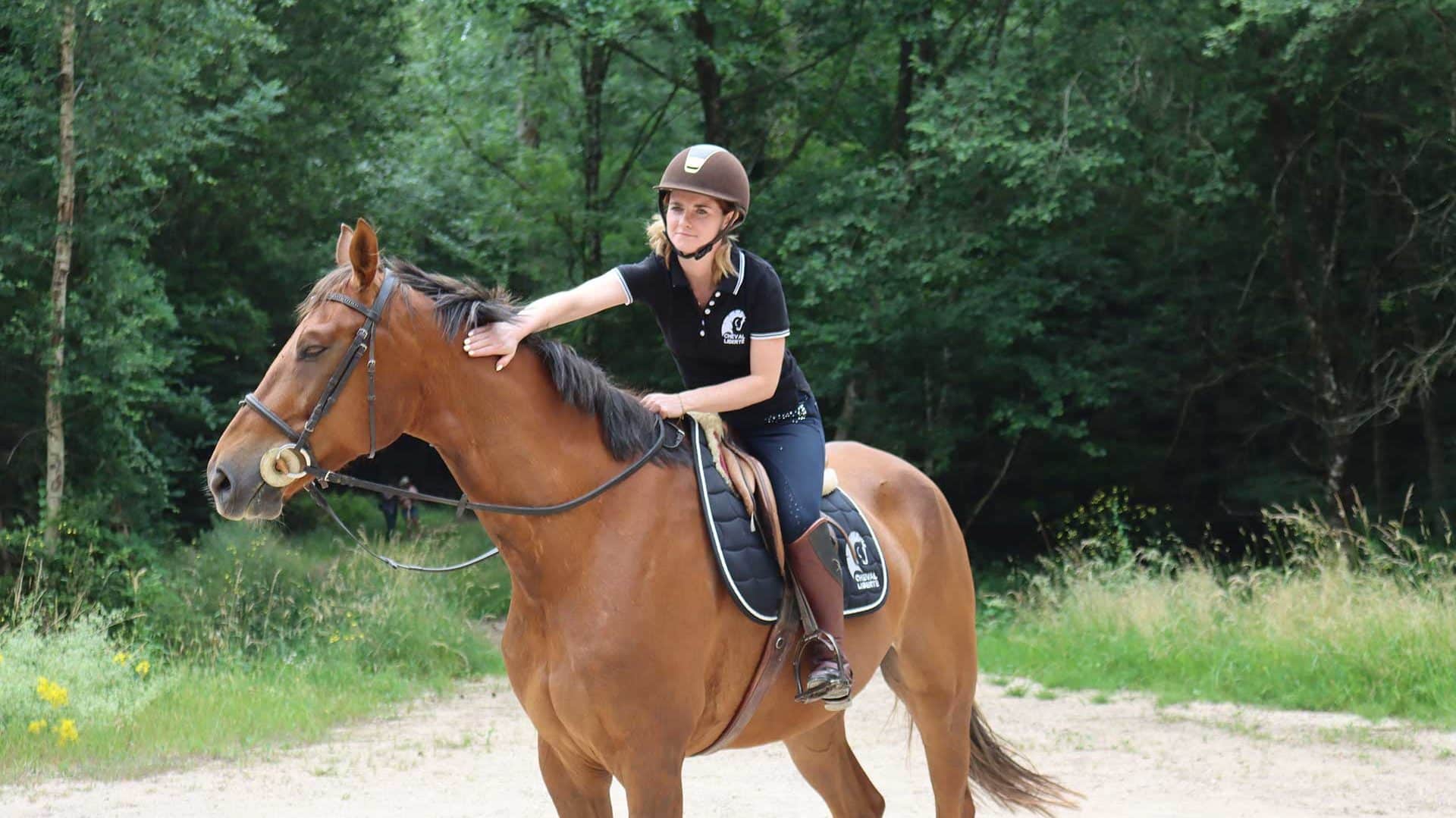 A stationary rider caresses her horse in the forest with a smile.